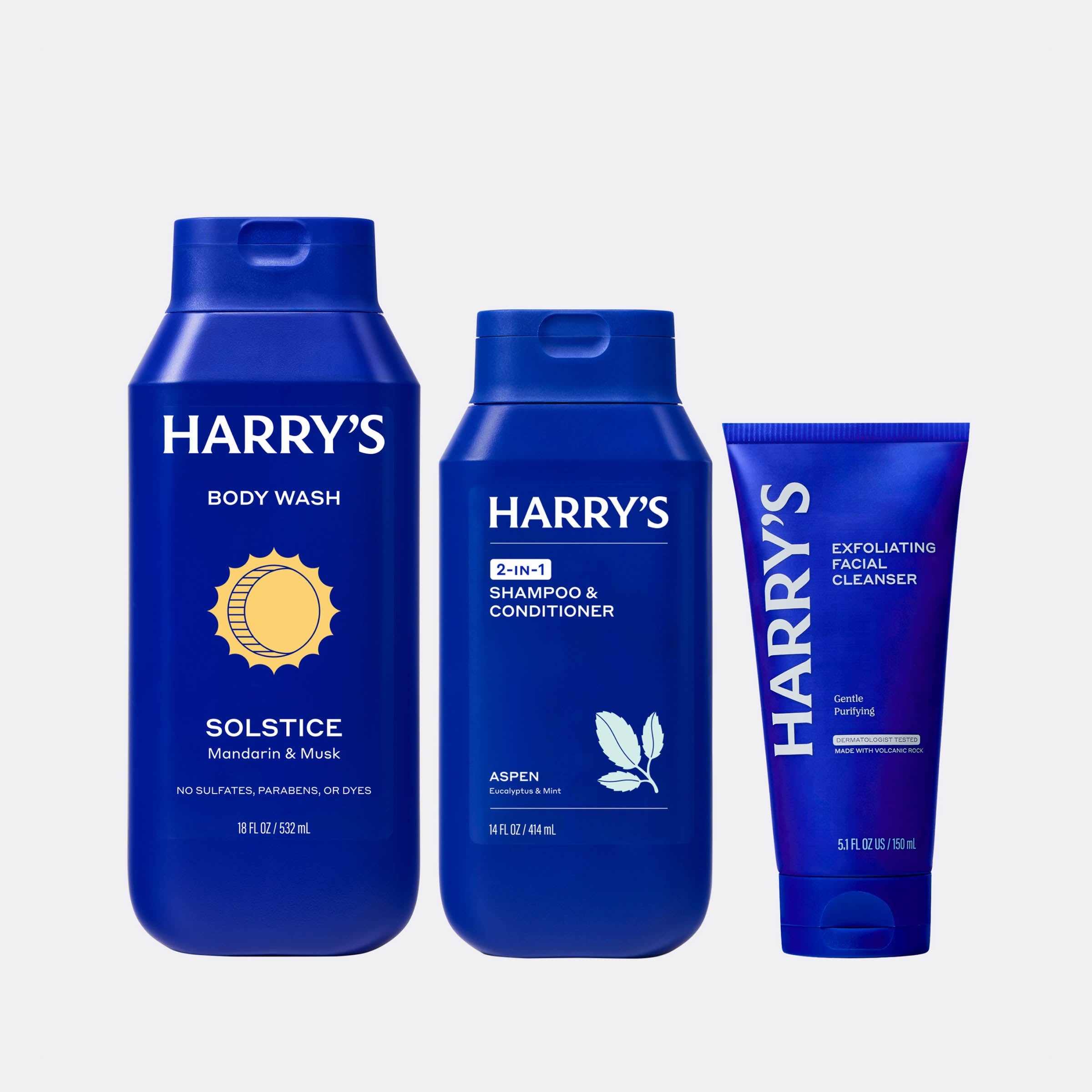 Three blue bottles of Harry's body wash, shampoo & conditioner, and facial cleanser on a light gray background