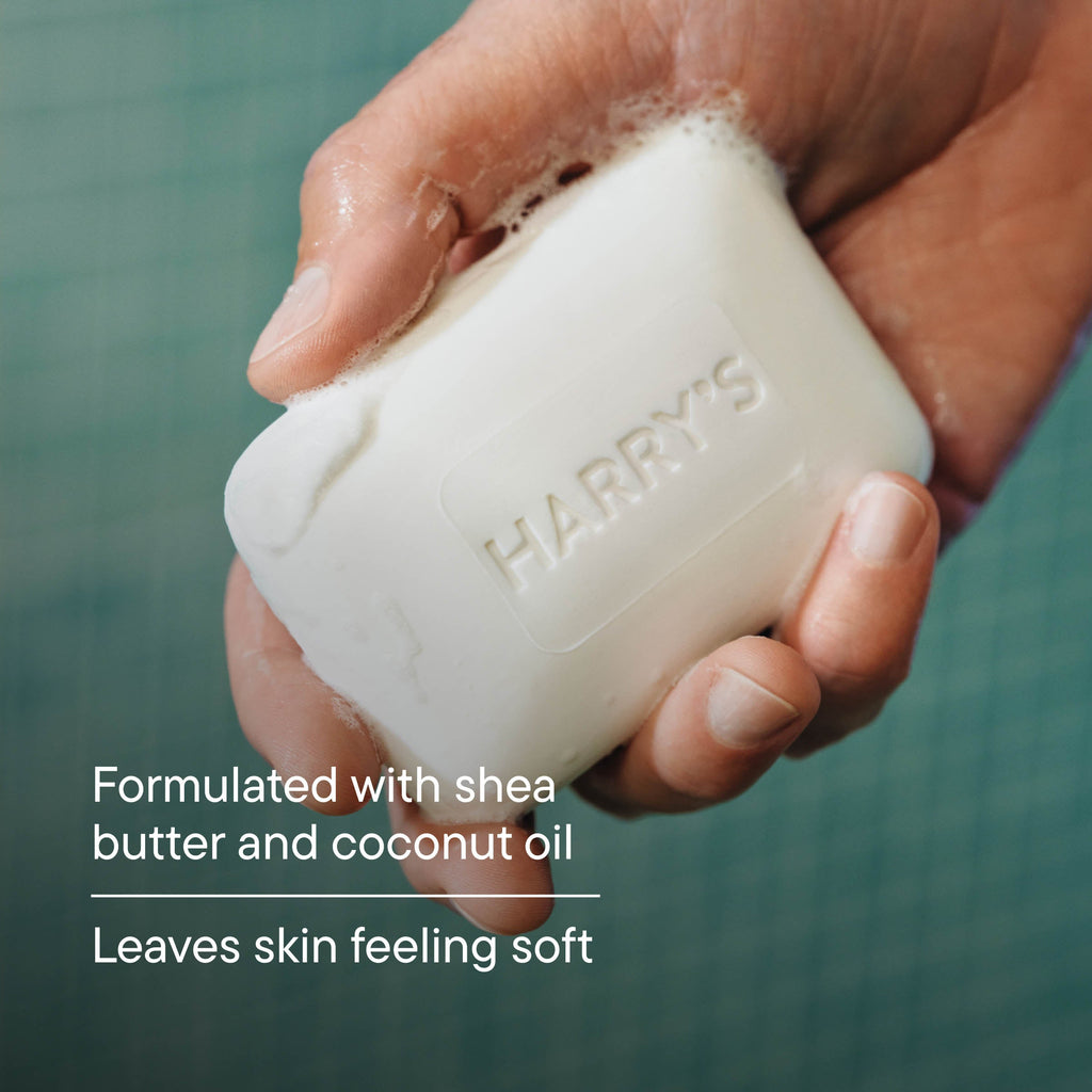Hand holding a bar of soap with 'HARRY'S' branding, against a green background.