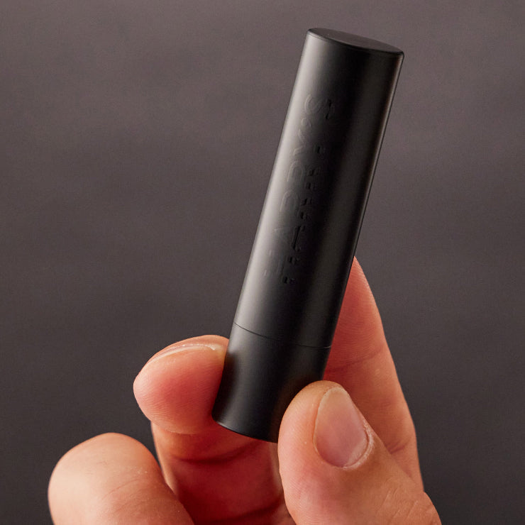 Black lip balm held in a hand against a dark background