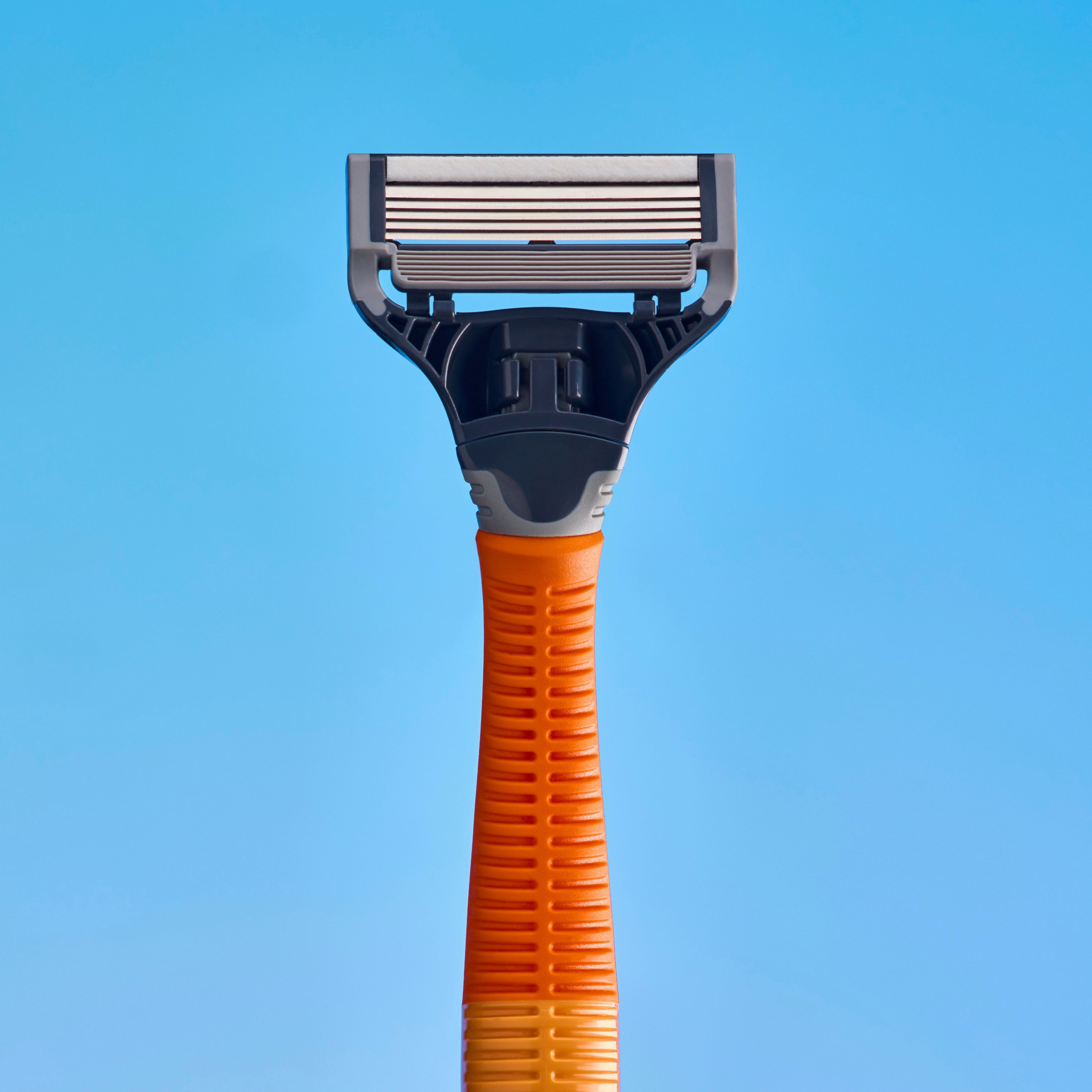 A close-up of a manual shaving razor with a textured orange handle and a dark gray and silver blade head, set against a solid blue background.