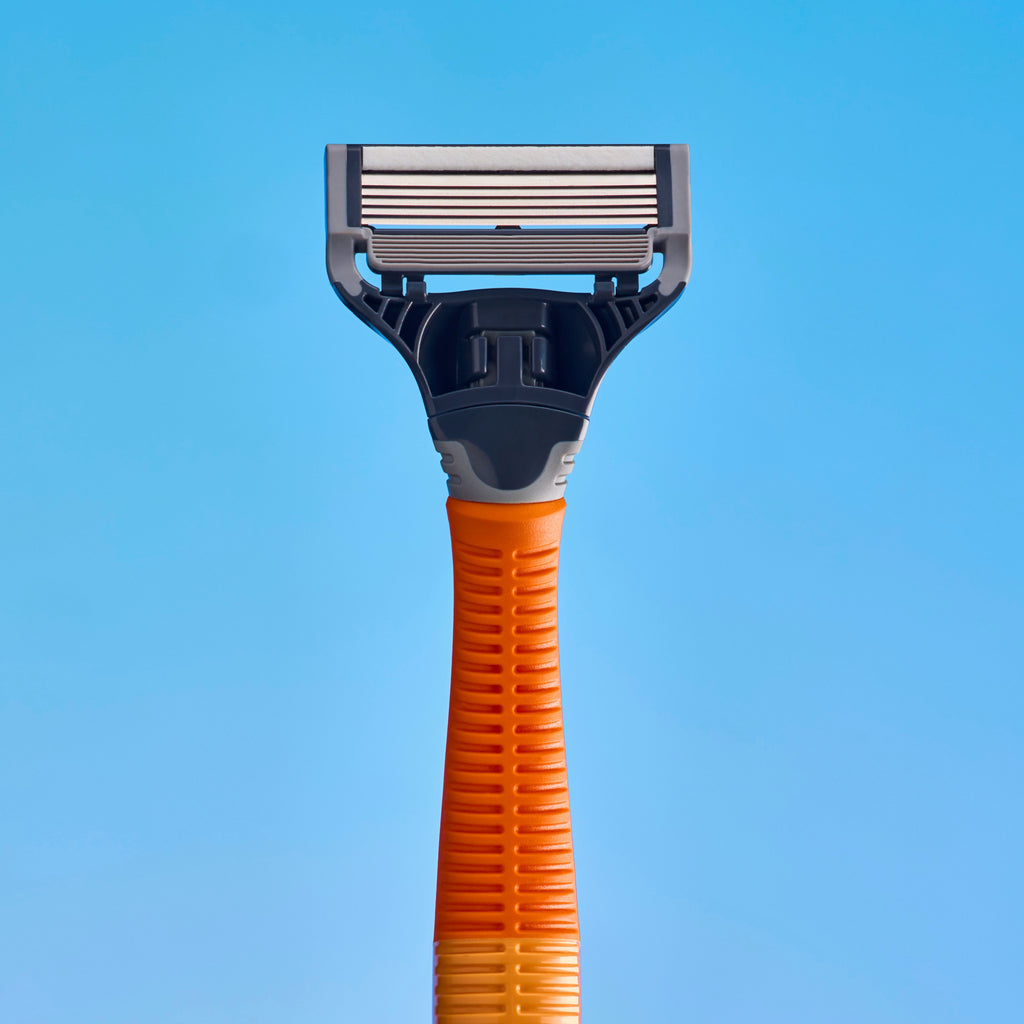 A close-up of a manual shaving razor with a textured orange handle and a dark gray and silver blade head, set against a solid blue background.