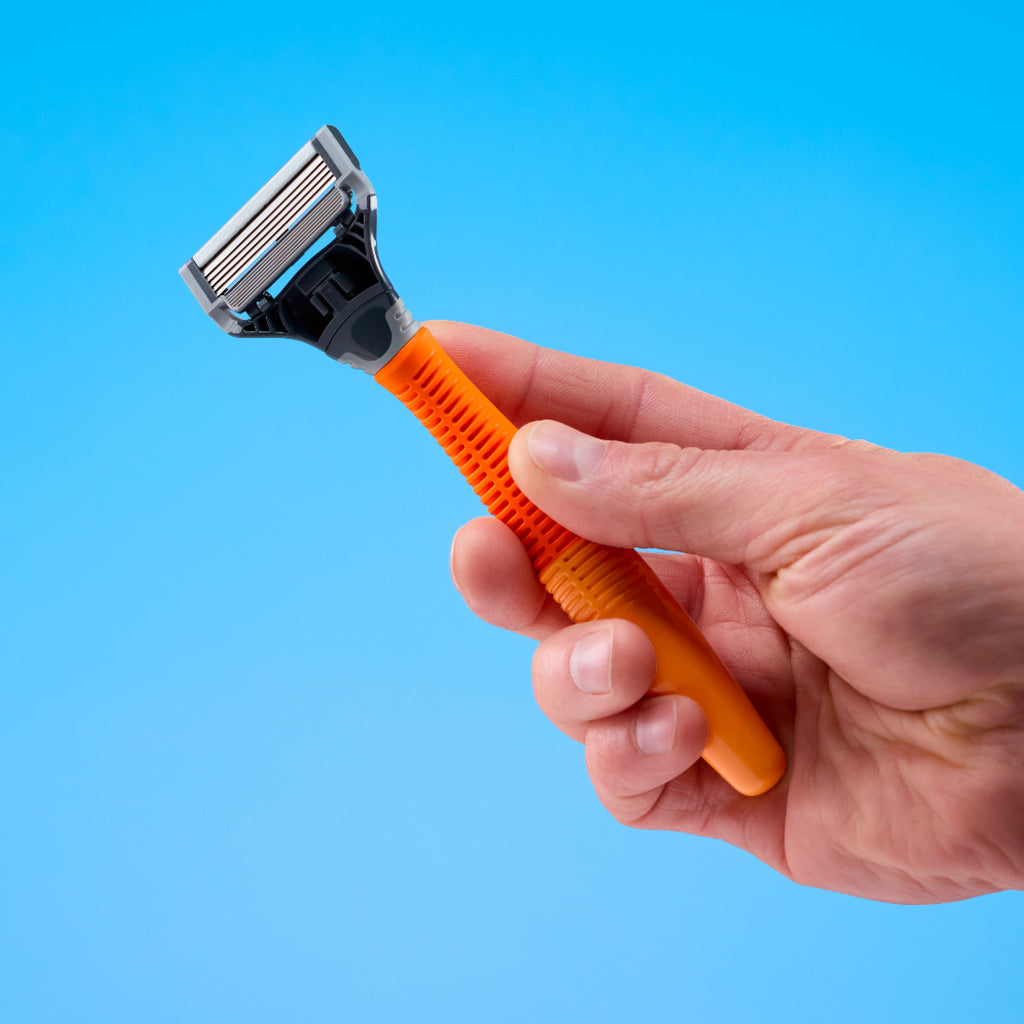 A hand holding a multi-blade razor with an orange textured handle and a silver and black head, set against a solid blue background.