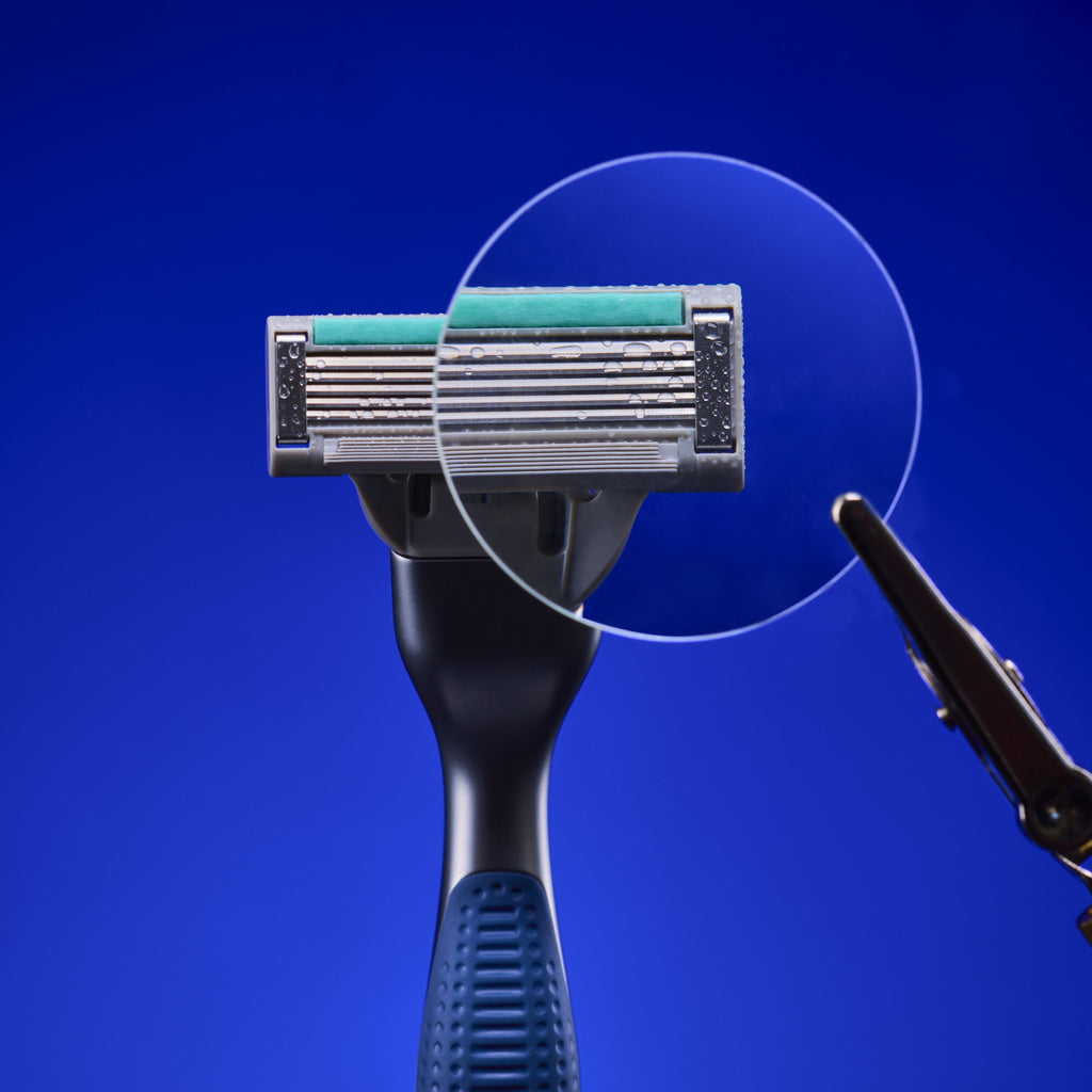 A close-up of a multi-blade razor with a dark handle and metallic head, shown against a solid blue background with a circular transparent overlay highlighting the blade area.